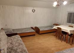 Pokój o jasnych ścianach, a w nim kanapa, dwa łóżka, stół i krzesła