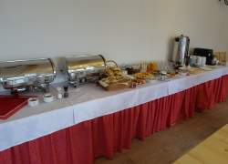 Jadalnia - widoczny stół przykryty długim czerwonym obrusem, na wierzch którego położono mniejsze obrusy białe, na stole szwedzki bufet - śniadanie; widoczny termos, filiżanki, talerzyki, zimna płyta i dwa podgrzewacze do potraw w kolorze srebrnym