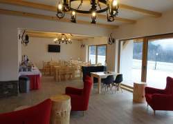 Jadalnia - widoczne czerwone fotele, krzesła i stoły z jasnego drewna, duże okna, telewizor, potężny kuty żyrandol