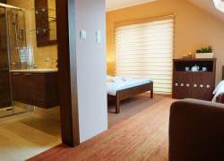 Widok na pokój i łazienkę, duże okno balkonowe; szafka z serwisem kawowym; łóżko małżeńskie.