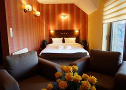 Łóżko małżeńskie, żółte róże na stoliku, dwa fotele beżowe.