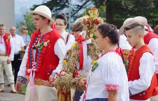 Ludzie w strojach regionalnych z koroną dożynkową