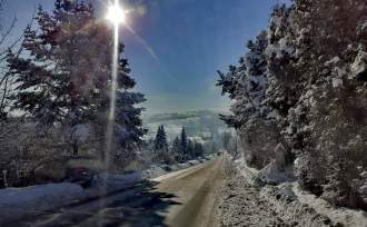 DW 941; widok drogi i chodnika przedstawiający ich zimowe utrzymanie; na zdjęciu widoczne drzewa, błękitne niebo