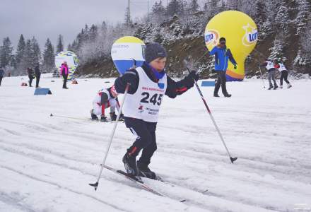 Chłopczyk z numerem startowym 245 – Rucki Paweł, w tle inni biegacze i balony promocyjne oraz ubrany w niebieską kurtkę mężczyzna