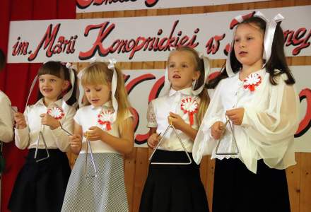 Dziewczynki z klasy pierwszej w czarno białych eleganckich strojach grające na trójkątach