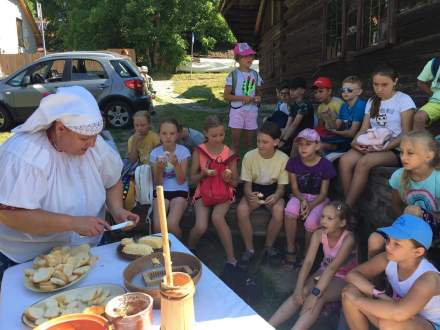 Dzieci przy Kurnej Chacie Kawuloka podczas degustacji jedzenia regionalnego serwowanego przez Panią w góralskim stroju