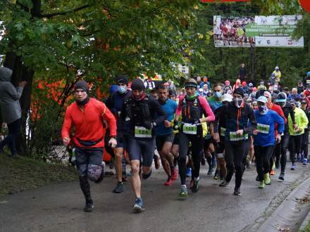 Grupa biegnących drogą ludzi w kolorowych ubraniach, nad drogą baner