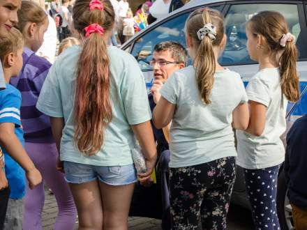 policjant wśród dzieci w tle samochód