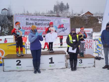 Dekoracja najmłodszych dziewcząt, na podium kolejno Partyka Lena, Michałek Oliwia i na miejscu trzecim Legierska Milena; w rękach Leny Partyki kabotek; na zdjęciu widoczna Wójt Gminy Istebna – Łucja Michałek, Dyrektor Gminnego Ośrodka Kultury Łucja Dusek