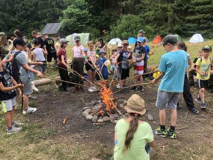 Duża grupa dzieci piekących kiełbaski nad ogniskiem.
