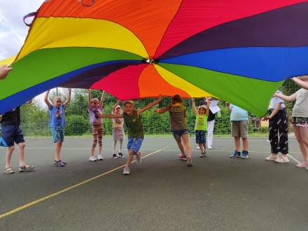 Barwna chusta animacyjna rozpostarta przez bawiące się na boisku dzieci.