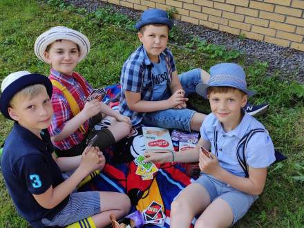 Czterech chłopców w kapeluszach siedzi na kocu na trawie