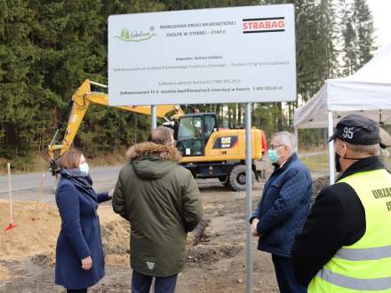 Tablica informująca o inwestycji, a przed nią Wójt Gminy Istebna, Stanisław Szwed - Wiceminister Rodziny i Polityki Społecznej, , Grzegorz Puda-  Minister Rolnictwa i Rozwoju Wsi oraz Przewodniczący Rady Gminy Istebna