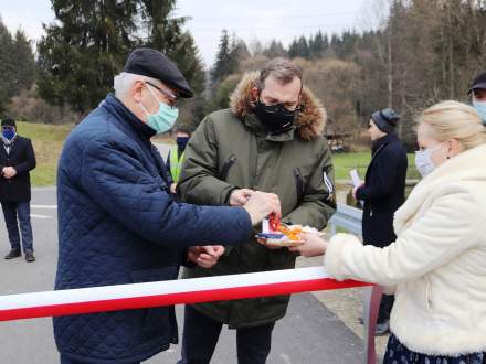 Stanisław Szwed i Grzegorz Puda odbierają nożyce do przecięcia wstęgi z rąk ubranej w strój regionalny Małgorzaty Owczarczak