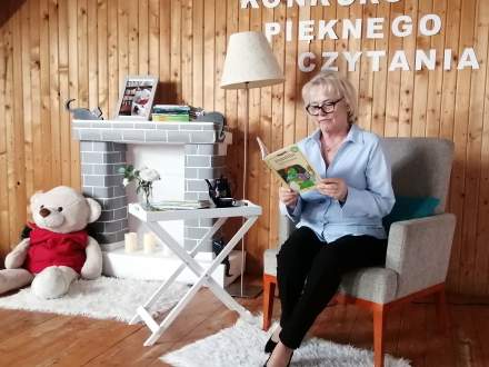 Konkurs Pięknego Czytania w SP2 Istebna; nauczycielka w fotelu z książką; w tle kominek i miś zabawka