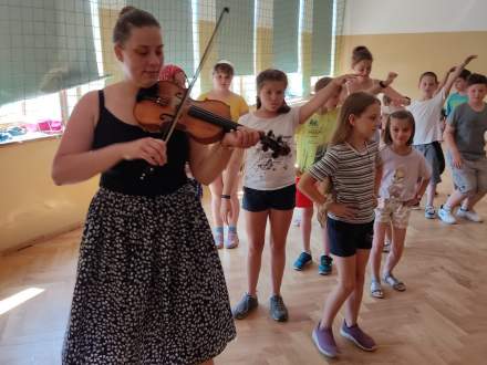 Dziewczyna grająca na skrzypcach; wkoło tańczące dzieci
