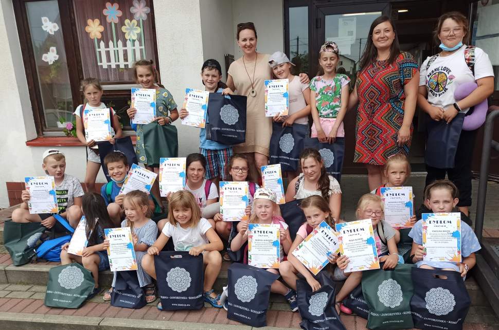 fot. Edyta Kukuczka; na zdjęciu dwie nauczycielki i grupa dzieci siedzących lub stojących na schodach szkoły; dzieci mają granatowe i zielone torebki z upominkami oraz kolorowe dyplomy